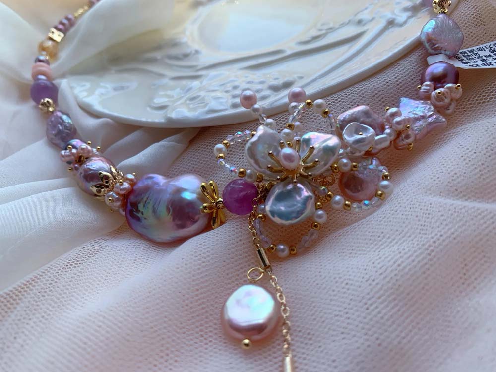 Lavender and pink freshwater baroque pearl necklace featuring a central floral motif and pearl pendant drop.